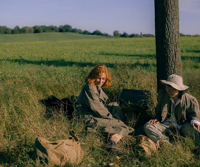 Two people sitting against a grassy field
