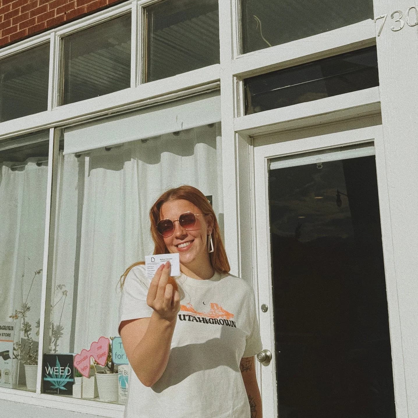 Smiling person with sunglasses holding a medical wellness card